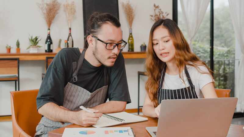 Small business owners couple using laptop discussing financial documents