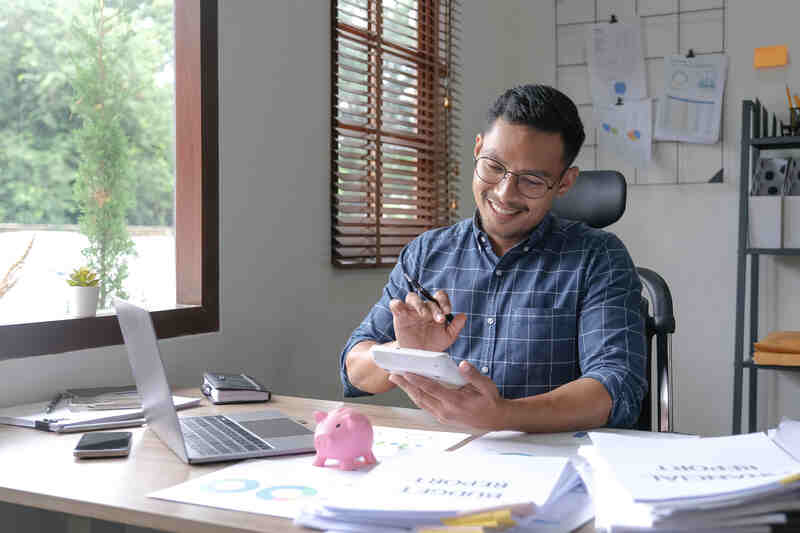 Male small business owner using a calculator and a laptop