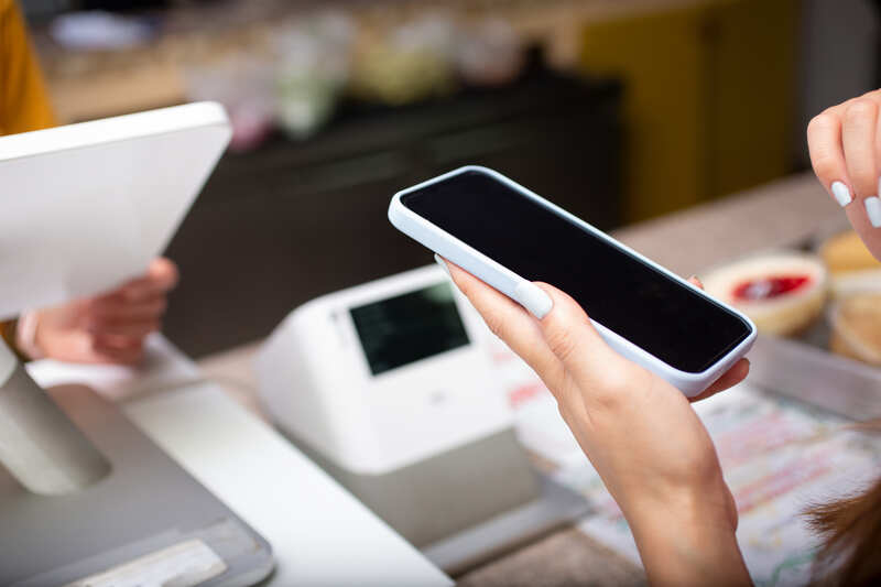 A view of a person holding up a cell phone at the cash register of a retail store
