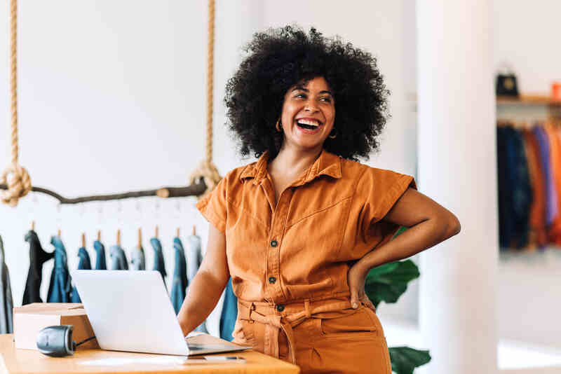 Female small business owner smiling cheerfully in her shop with a laptop