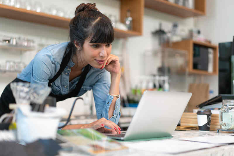 small business coffee shop owner in apron checking online order from customer on computer