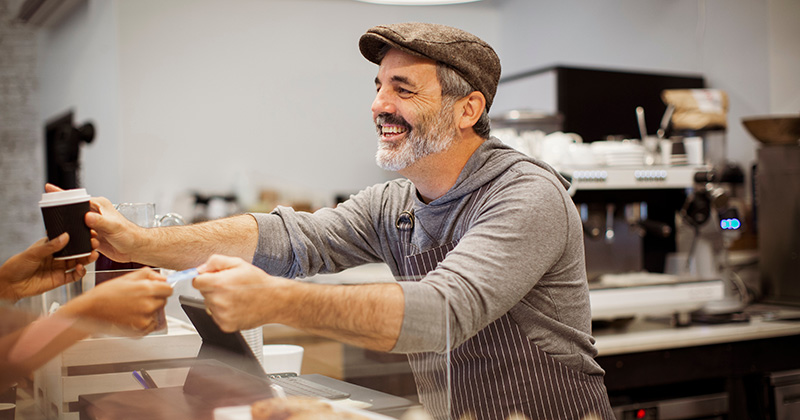 A coffee shop owner handing a customer a cup of coffee.
