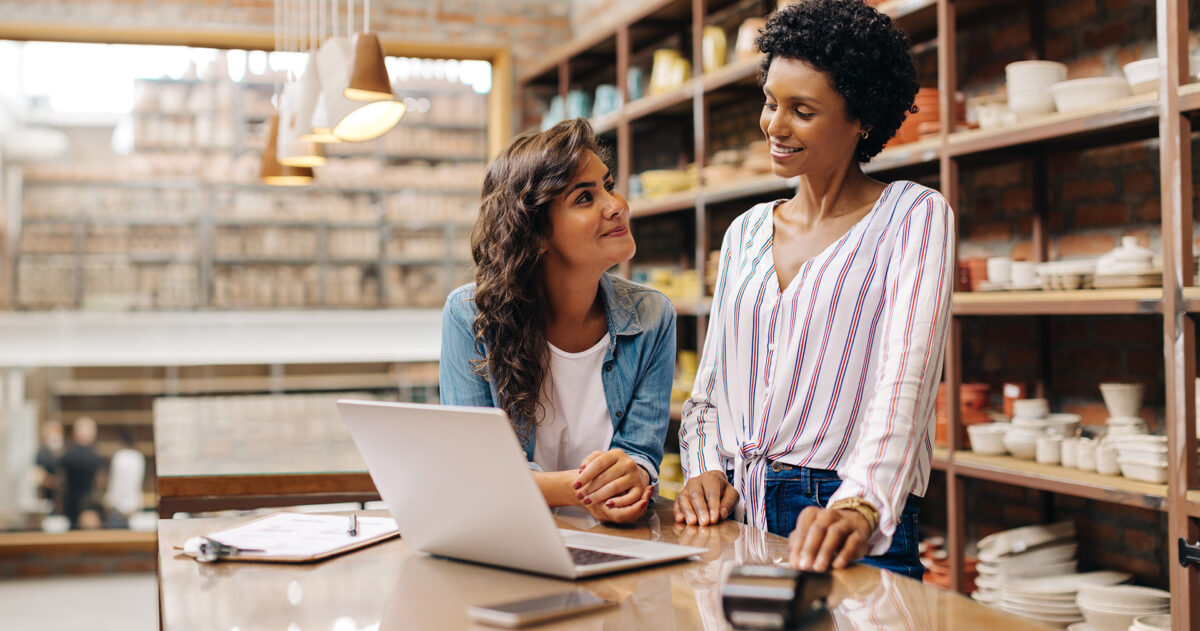Two female business owners work at a desk with a laptop.