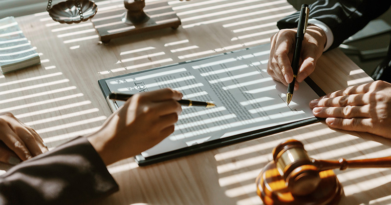 Close up shot of a legal document on a desk with two peoples arms in frame.