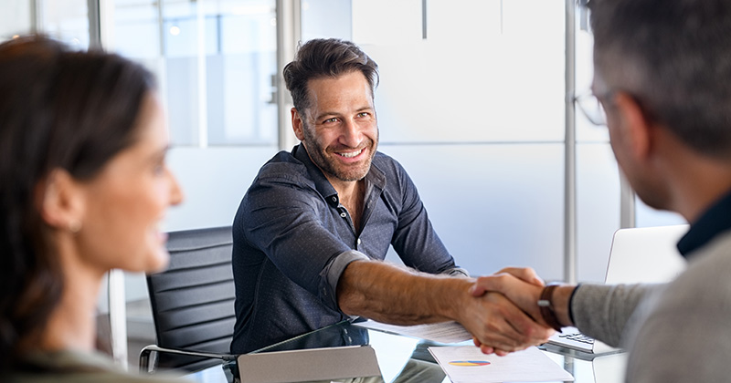 Two men shaking hands over a table.