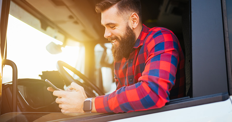Young-handsome-bearded-truck-driver-using-smart-phone-in-his-truck.
